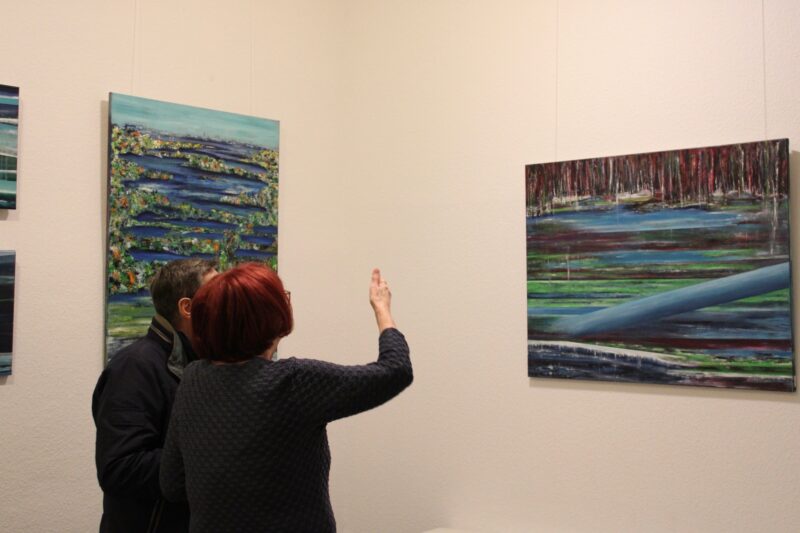 Zwei Besucher*innen bei der Kunstausstellung "Form des Wassers" vor einem Ölgemälde.